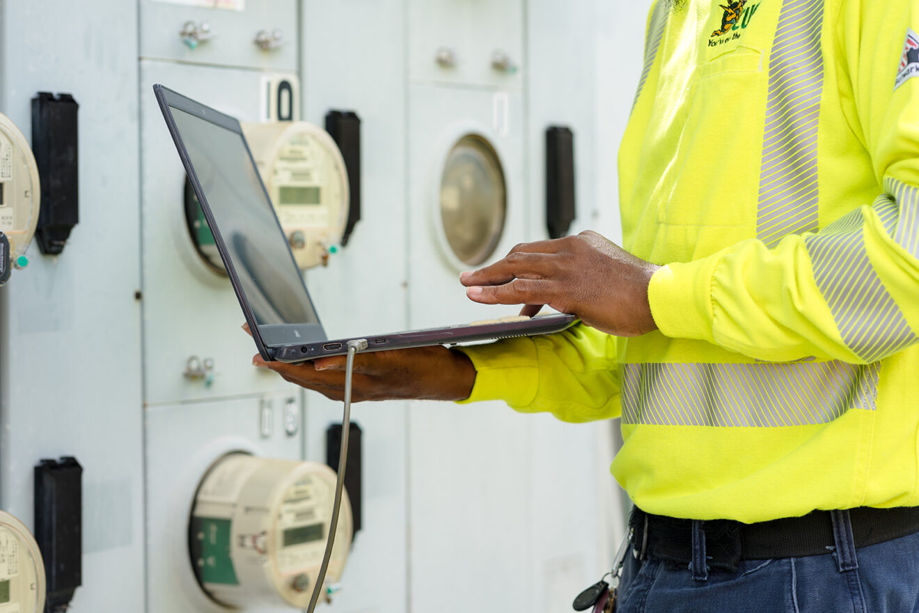 Utility worker on a laptop measuring energy usage from an electricity meter