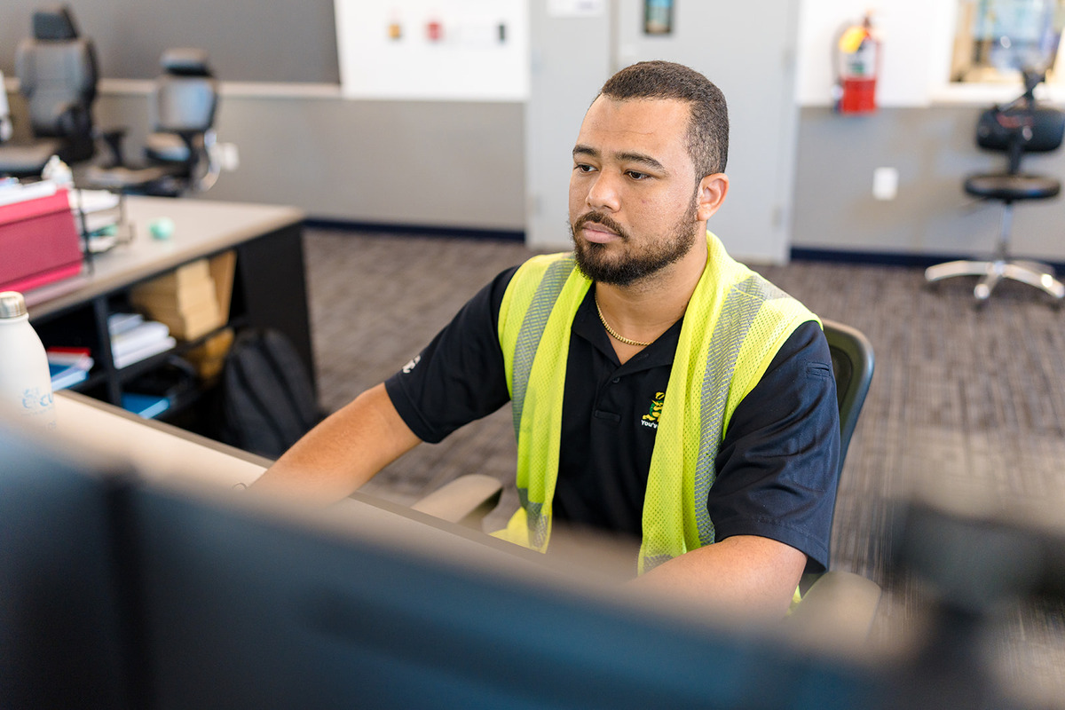 CUC staff member wearing a safety vest working at a computer in a control room or office environment, focused on monitoring or administrative tasks.