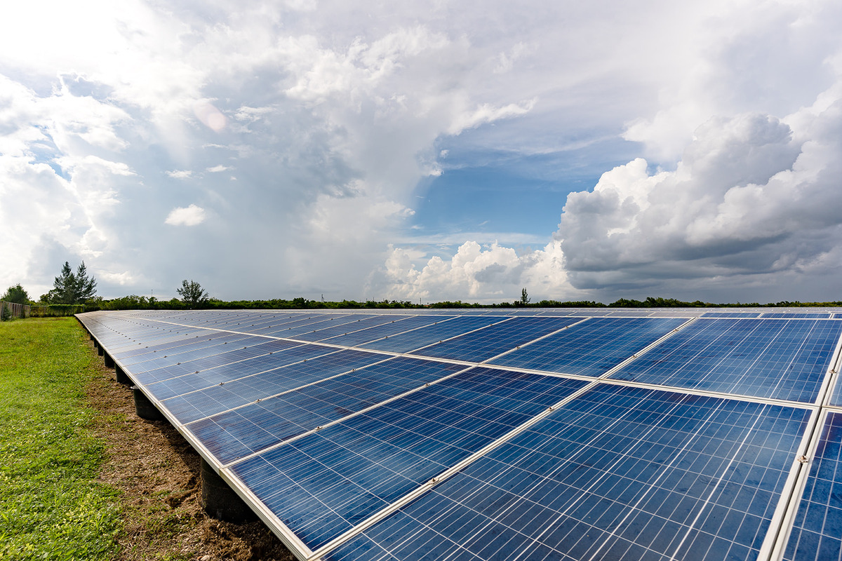 Wide view of a solar panel array installed in a grassy field under a partly cloudy sky, representing renewable energy and sustainable power generation.